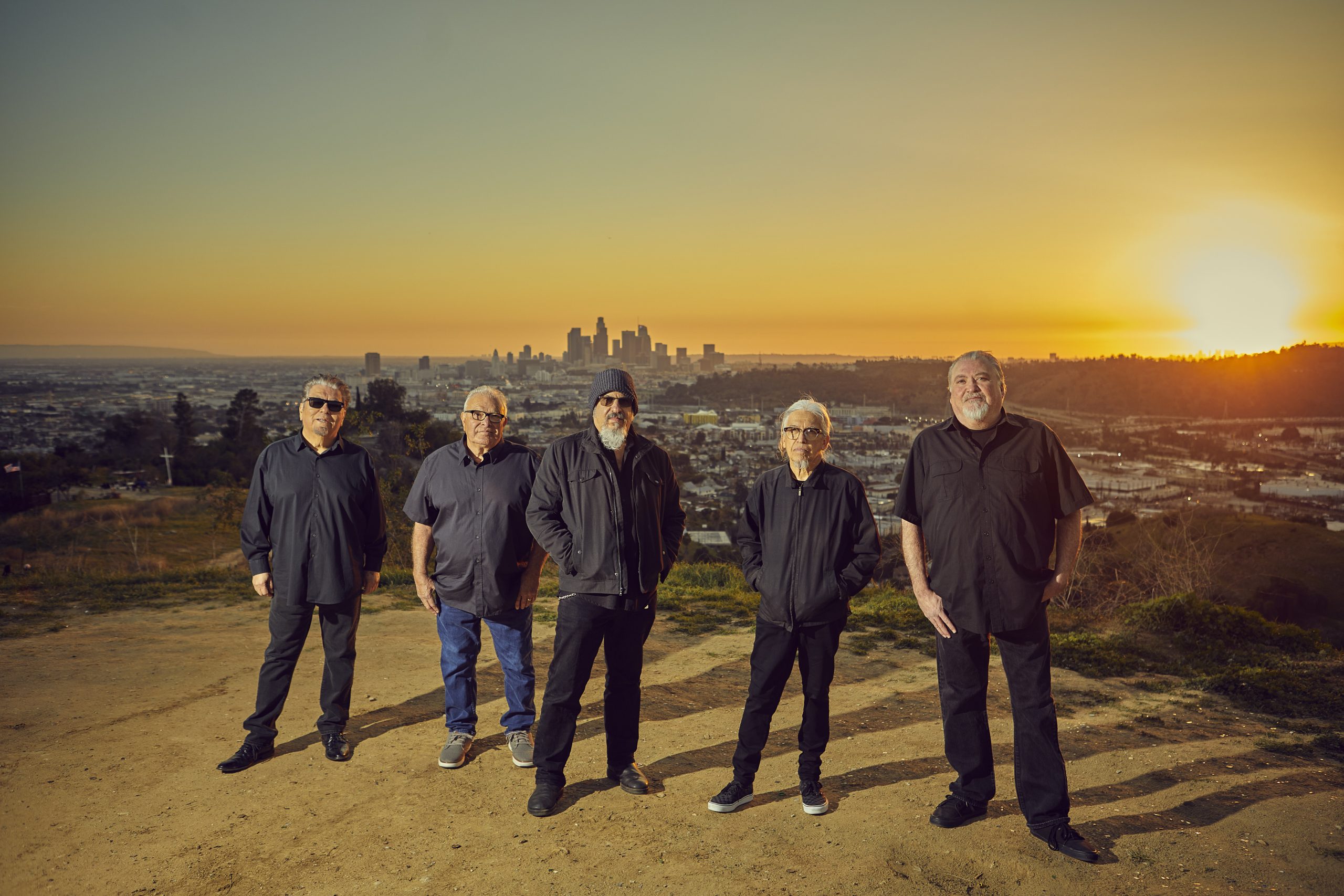 The Los Lobos band standing in front of a sunset